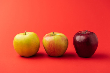 row of three ripe multicolored apples on red background