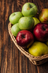 wicker basket with tasty multicolored apples on wooden table