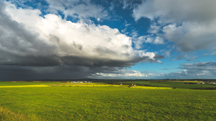 Fototapeta premium Heavy rainy clouds over the Northern Ireland field. Stunning countryside landscape. Green grass covered meadow under the colorful sky before the rain. Panoramic view of the wild virgin nature.