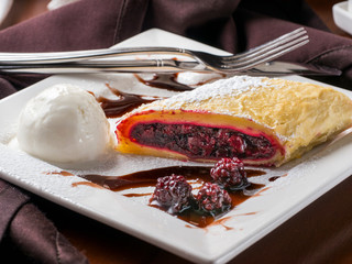 Sweet dessert - strudel with cherry and blackberry on white plate with ice cream at restaurant table
