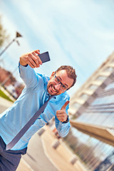 Funny businessman with thumbs up while using smartphone outdoors.