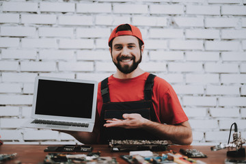 Young Man in Red Cap with Fixed Laptop in Workshop