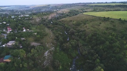 Aerial shot of a snaky river flowing between rugged banks with cane in summer