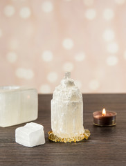 Naturally carved mineral stone Selenite tower has healing on cleansing properties. Candle holder, piece of raw and carved Selenite tower on dark wooden table, orange bokeh background.