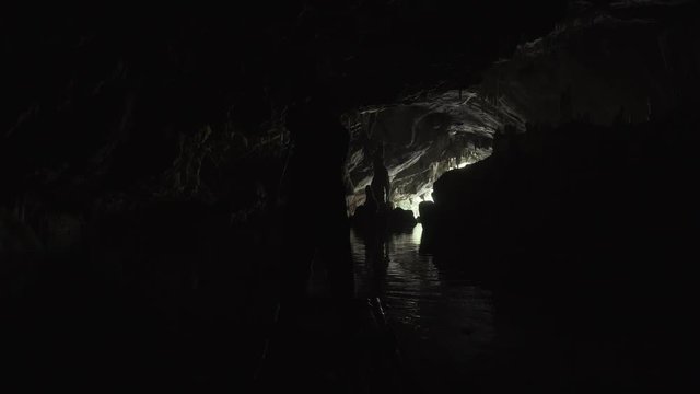 Silhouette of a man floating on the river in a dark cave on a bamboo raft towards the exit. Lod Cave. Thailand.