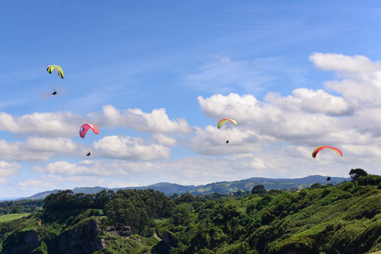 Paragliders against cloudy sky over green countryside