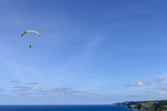 Paragliders against cloudy sky over green countryside