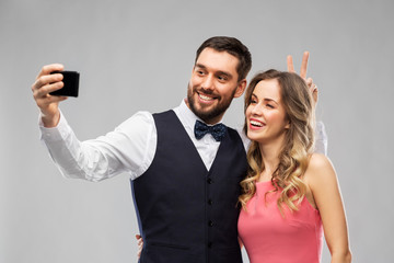 technology and people concept - happy couple in party clothes taking selfie by smartphone over grey background