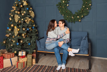 Obraz premium attractive couple sitting on a sofa tenderly embracing with a Christmas tree in the background