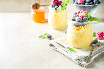 Healthy diet good ideas, sweet breakfast polenta in portioned jars with fresh frozen berries and honey, beige stone background copy space top view
