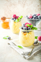 Healthy diet good ideas, sweet breakfast polenta in portioned jars with fresh frozen berries and honey, beige stone background copy space top view