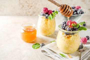 Healthy diet good ideas, sweet breakfast polenta in portioned jars with fresh frozen berries and honey, beige stone background copy space top view