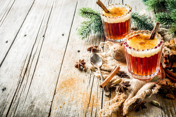 Winter holidays traditional drink, homemade hot buttered rum with spices, over old rustic wooden background with christmas tree branches, copy space - obrazy, fototapety, plakaty