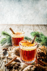 Winter holidays traditional drink, homemade hot buttered rum with spices, over old rustic wooden background with christmas tree branches, copy space