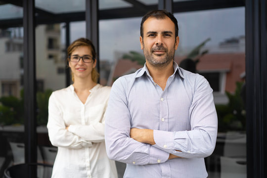 Portrait of confident mid adult male leader with female colleague. Caucasian entrepreneur standing and looking at camera, female employee standing behind. Business leader concept
