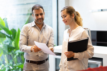 Portrait of smiling executive showing document to his secretary. Mid adult Caucasian businessman discussing paper with female colleague. Business relationships concept