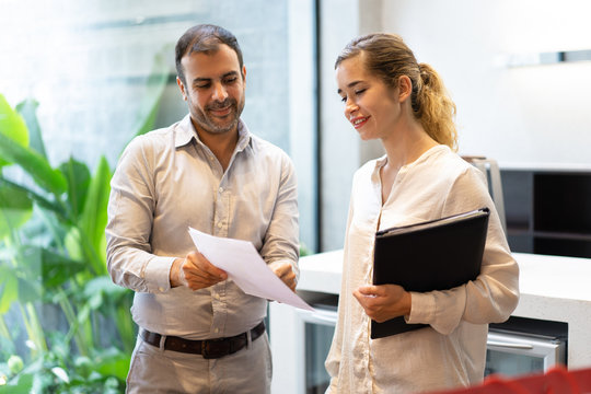 Portrait of smiling executive showing document to his secretary. Mid adult Caucasian businessman discussing paper with female colleague. Business relationships concept