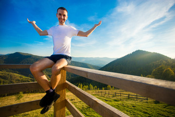 Fototapeta na wymiar Young tourist man on wooden balcony rejoicing wonderful view of mountains