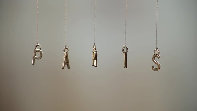 word "paris" made of metal letters hanging on ropes with blurred background