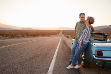 Senior couple on road trip standing by car, full length
