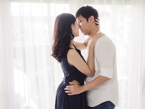 Romantic Asian couple hug and kissing near window at home, lifestyle concept.