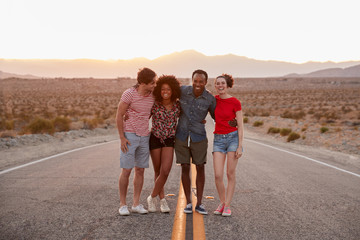 Four friends standing on a desert highway looking to camera