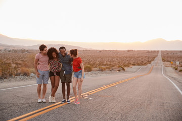 Fototapeta premium Four young adult friends standing on desert highway talking