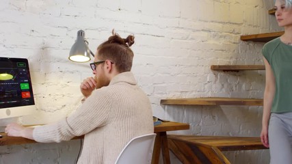 Tracking shot of young woman with short blue hair walking down stairs in modern loft apartment and hugging her boyfriend sitting at desk and working with graphs and charts on computer - Powered by Adobe