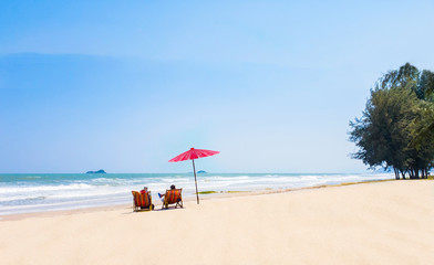summer couple of Middle-aged 40-50s on the beach vacation holiday relax on their  chairs under a red umbrella.  travel concept at Hua Hin Prachuap Khiri Khan in Thailand.Shoot photo by smart phone