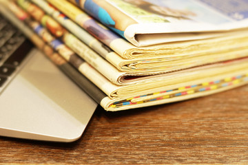 Newspapers and laptop. Pile of daily papers with news on the computer. Pages with headlines, articles folded and stacked on keypad of electronic device. Modern gadget and old journals, focus on paper 