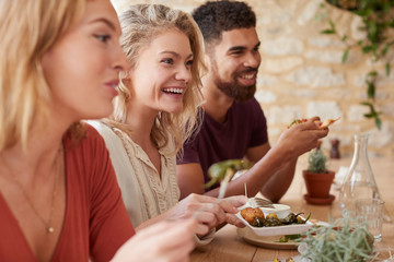 Three young adult friends eating in a restaurant, close up