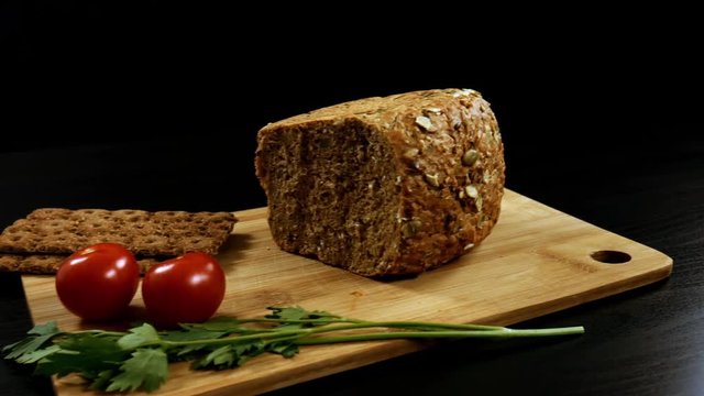 Healthy breakfast. Fresh grain bread, ripe cherry tomatoes and bread crips with parsley on the cutting board. Camera moves from right to left