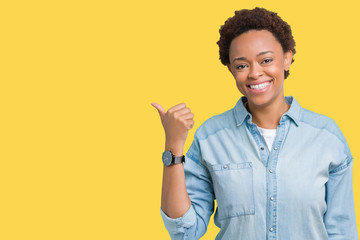 Young beautiful african american woman over isolated background smiling with happy face looking and pointing to the side with thumb up.