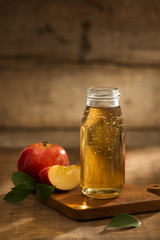 Apple juice in a bottle and glass with sliced red apple in wooden background