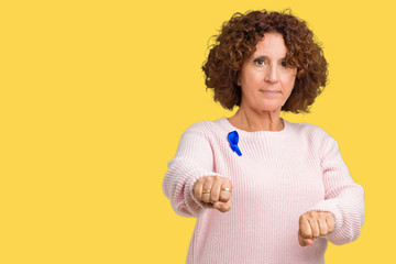 Middle ager senior woman wearing changeable blue color ribbon awareness over isolated background Punching fist to fight, aggressive and angry attack