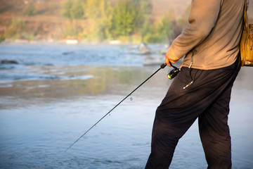 The fisherman catches fish on the shore of the lake, holds his hands spinning against the beautiful lake and cloudy sky.