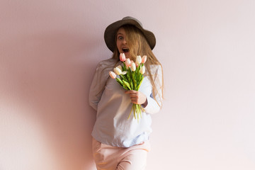 A young beautiful girl with blond dissolved long hair, a felt hat on her head, keeps spring flowers in her hands on a sunny day. Women's Day.