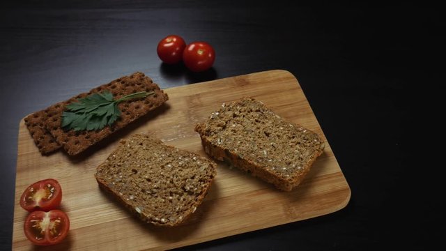 Healthy breakfast. Fresh grain bread,  ripe cherry tomatoes and bread crips with parsley on the cutting board. Camera moves from left to right
