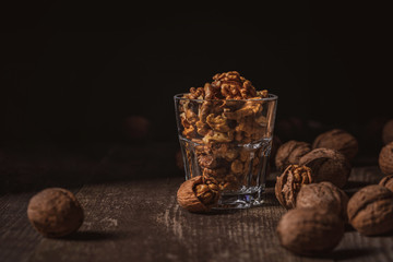 close up view of shelled walnuts in glass on wooden tabletop on black background