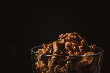 close up view of shelled walnuts in glass on black background
