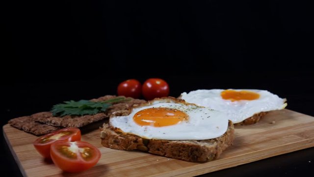 Healthy breakfast. Scrambled eggs on a fresh grain bread, ripe cherry tomatoes and bread crips with parsley on the cutting board on the table. Camera moves from left to right