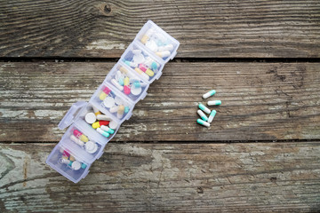 Variety of pills in white plastic pill organizer on weathered wood