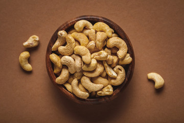 top view of cashew nuts in wooden bowl on brown background