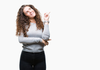 Beautiful brunette curly hair young girl wearing a sweater over isolated background with a big smile on face, pointing with hand and finger to the side looking at the camera.