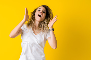 Beautiful young blonde woman jumping happy and surprised over isolated yellow background