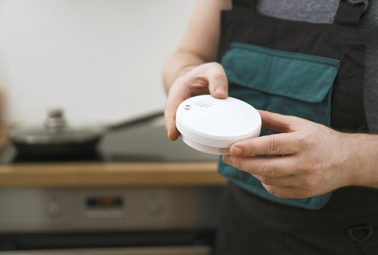Man holding smoke detector in the kitchen.