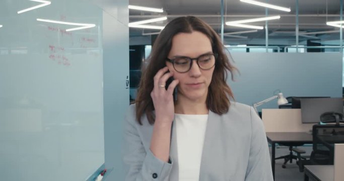 TRACKING Mid 30s Caucasian woman executive walking through an empty office, talking on the phone. 4K UHD