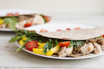 Healthy salad with chicken breast, mushrooms, yellow bell pepper, parsley, arugula and cherry tomatoes in a whole wheat wrap and served on white plate