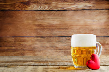 Glass of cold light beer with heart on a wood background for Valentine's day