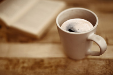 Mug cup of coffee and a book on a old wooden Table in a relaxing scenery in a vintage style photo